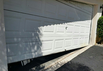Severely off track white garage door with visible dents, hanging unevenly at a North Saint Paul home.