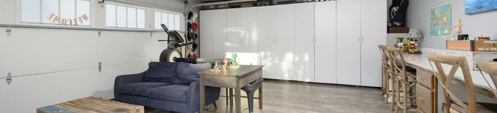 Spacious Mahtomedi garage transformed into a multi-purpose room with wall-to-wall storage cabinets, a cozy sofa, workout equipment, and a bar-height workspace.