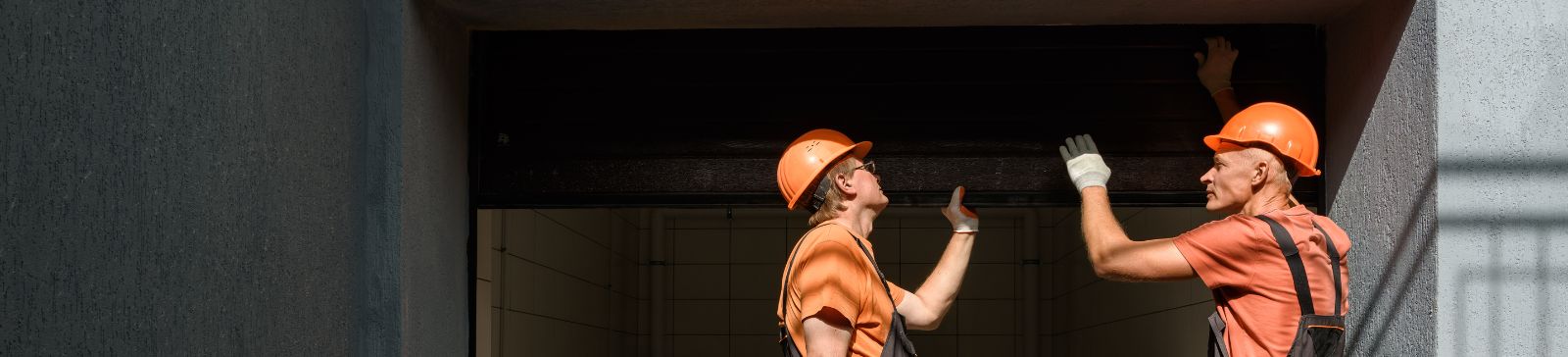 Two technicians in orange uniforms and hard hats inspecting a garage door installation inside a Mahtomedi home garage.