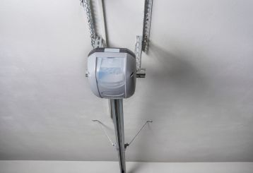 Close-up view of a modern automatic garage door opener mounted on the ceiling, showing the rail and motor system in a Mahtomedi garage.