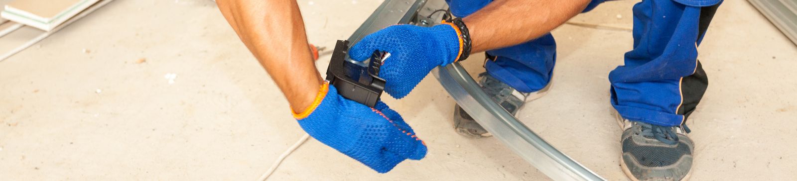Technician in blue uniform and gloves using a wrench to repair a curved garage door track on a job site in Mahtomedi, MN.