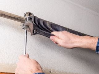 Garage Door Torsion Spring Repair – Mahtomedi, MN Close-up of a technician’s hands using a wrench and winding bar to adjust a black torsion spring on a residential garage door in Mahtomedi, MN.