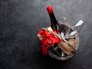 A romantic Valentine’s Day gift basket with wine, glasses, and heart-shaped décor set on a garage floor, ready for a special celebration.