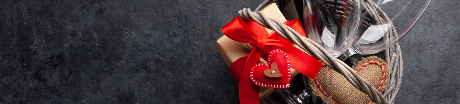 A romantic Valentine’s Day gift basket with wine, glasses, and heart-shaped décor set on a garage floor, ready for a special celebration.